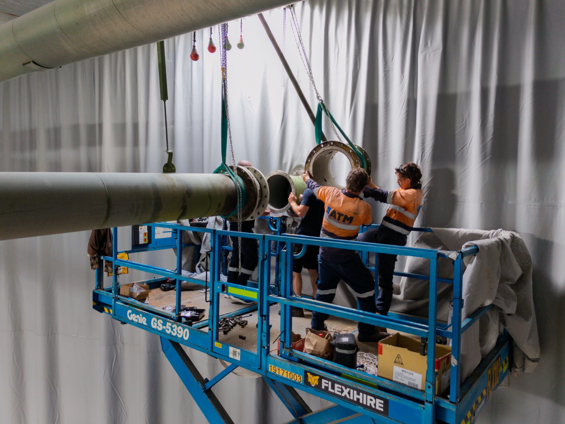 ATM Tanks — The crew guiding a suspended pipe section into place from a raised scissor lift inside the tank