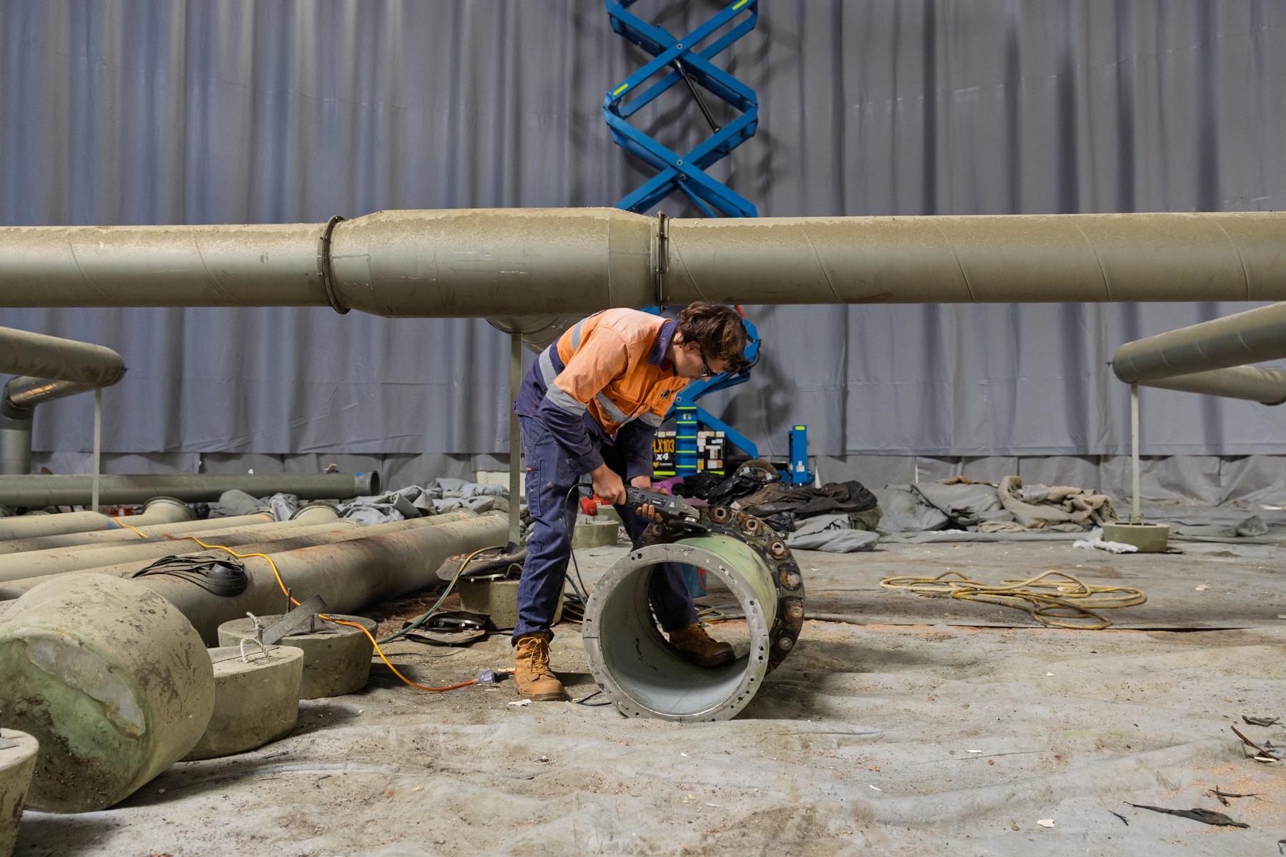 ATM Tanks — A worker cutting a pipe collar on the floor of the tank, with pipework laid out behind